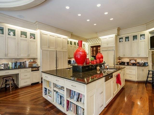 A large kitchen with a huge kitchen island with featuring built-in bookshelves, black countertops, and ample cabinet space